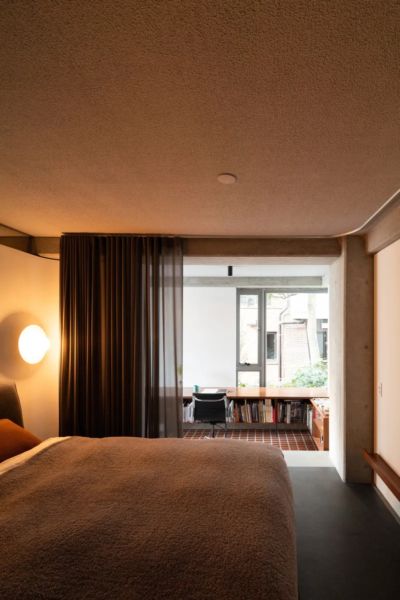 Bedroom with brown curtains dividing sleeping area from study nook with desk and bookshelves at window