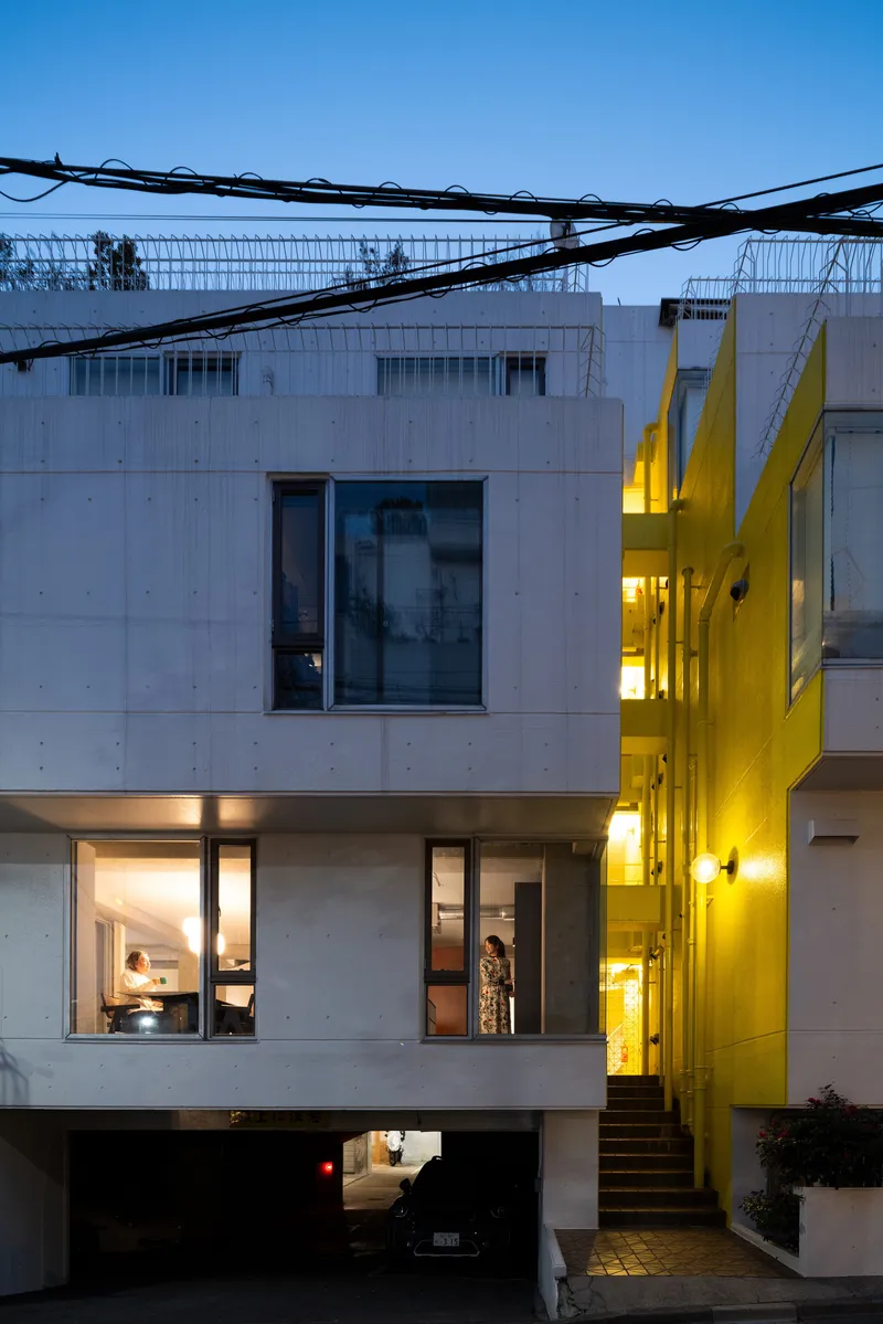 White concrete facade with staggered windows and yellow-lit exterior stair at twilight