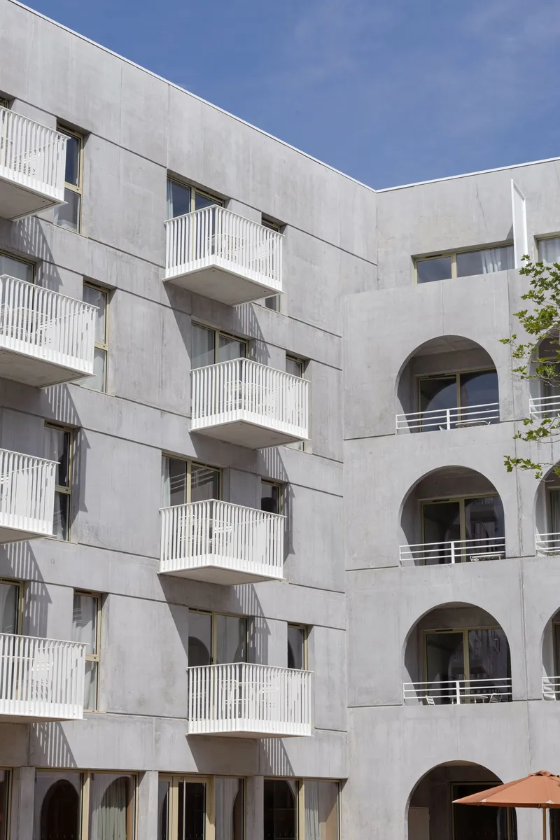 Courtyard view showing concrete balconies with vertical railings facing arched openings across the space