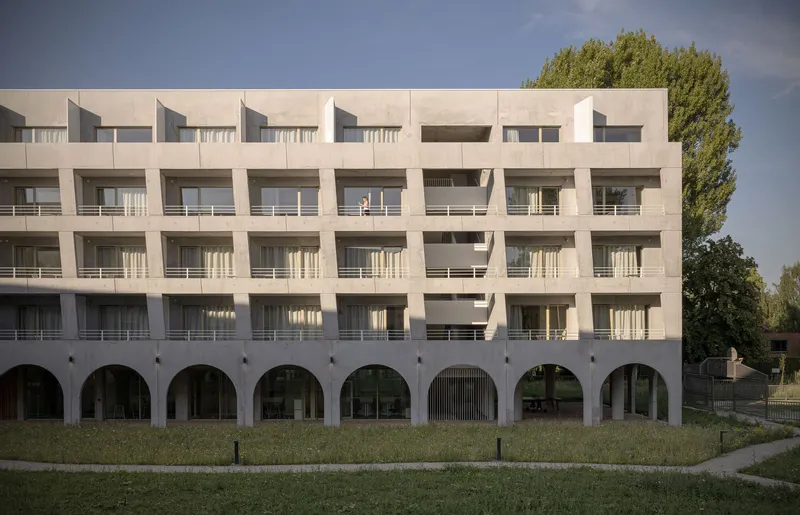 Street view of the white stucco facade with arched colonnade at ground level and tiered balconies above