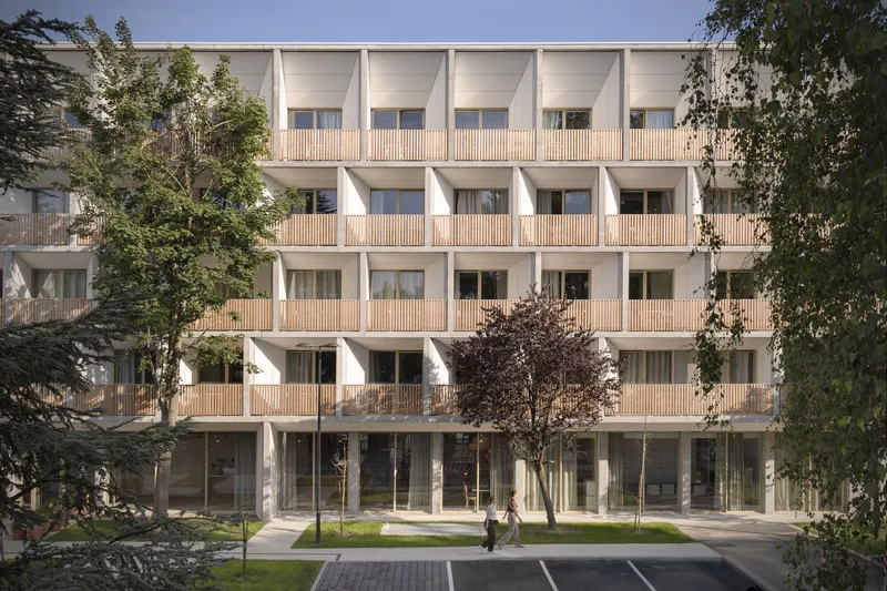 Courtyard facade with vertical timber battens screening balconies and young trees planted in the paved yard