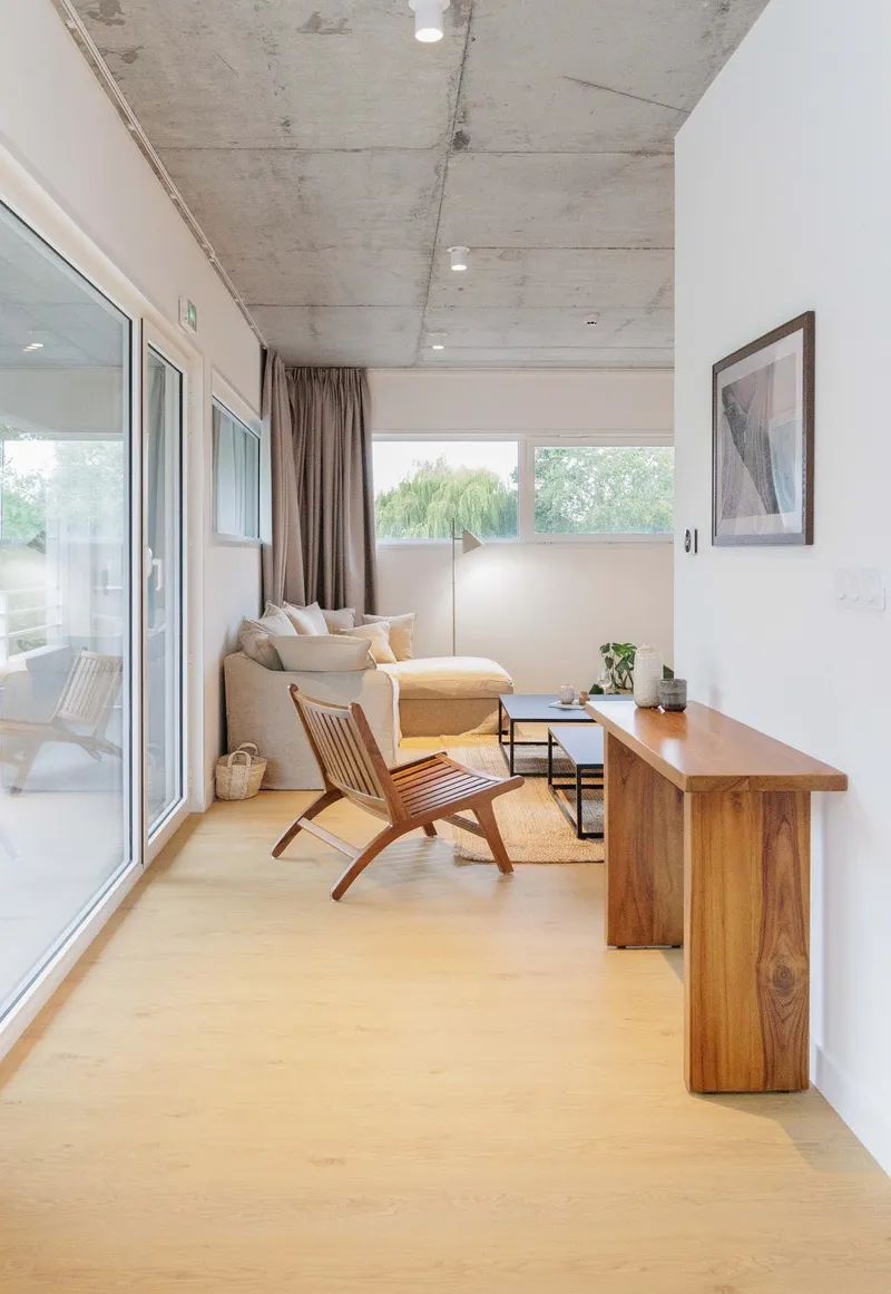 Living space with exposed concrete ceiling, pale timber floor, and glazed doors opening to a balcony