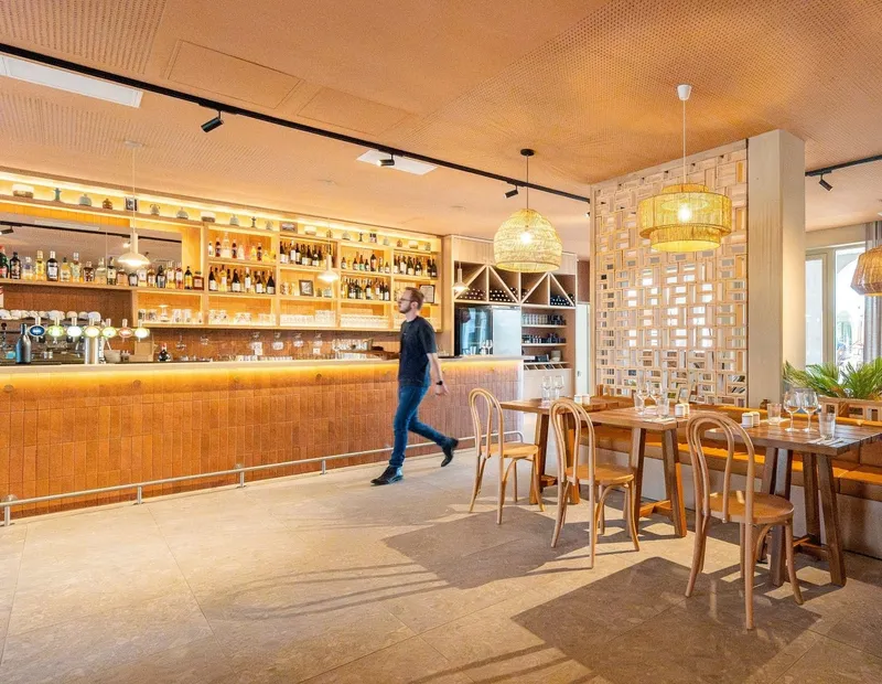 Restaurant interior with tiled bar counter, wicker pendant lights, and a person walking past dining tables