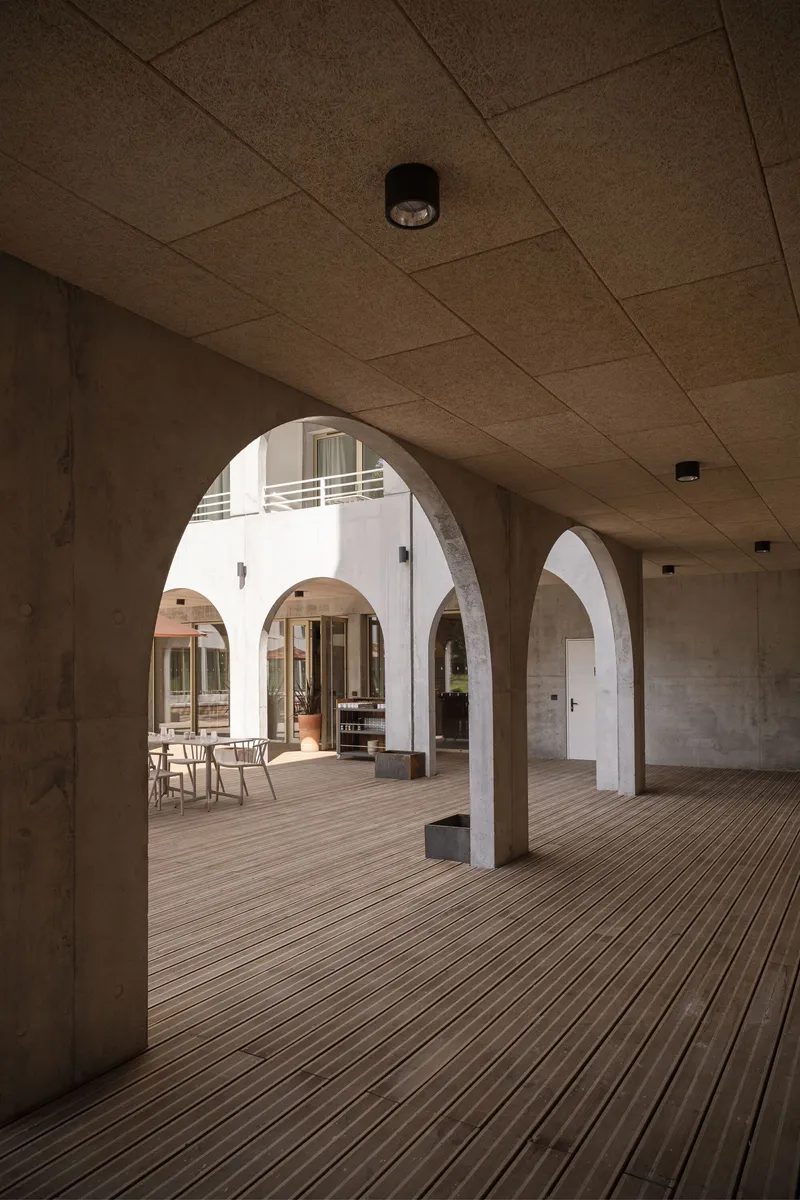 Arcade with rounded concrete arches, cork tile ceiling, and timber decking opening to a sunlit courtyard