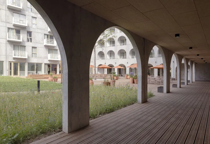Covered timber deck colonnade with concrete arches overlooking a planted courtyard and seating area