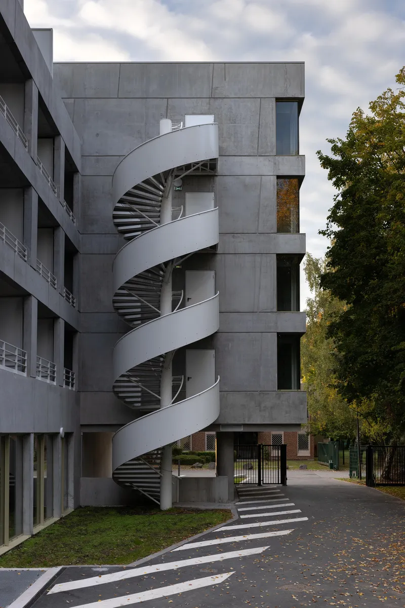 White helical exterior staircase wrapping around concrete tower beside a road with fallen autumn leaves