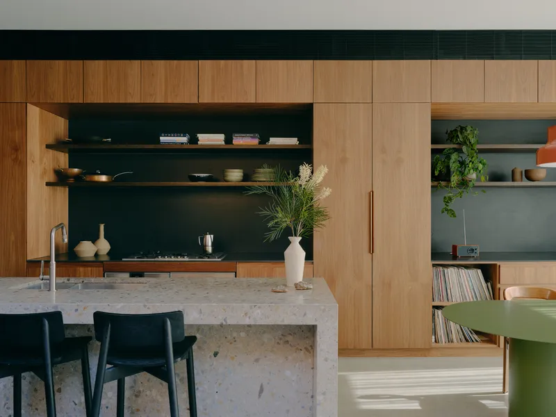Kitchen with terrazzo island bench, dark open shelving and timber ceiling band in natural light