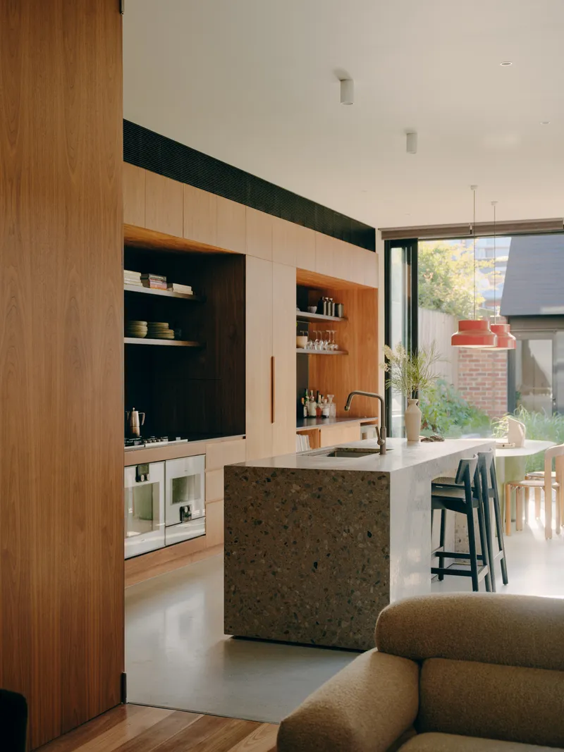 Interior kitchen view showing timber joinery, terrazzo waterfall island and courtyard glimpse through glazing