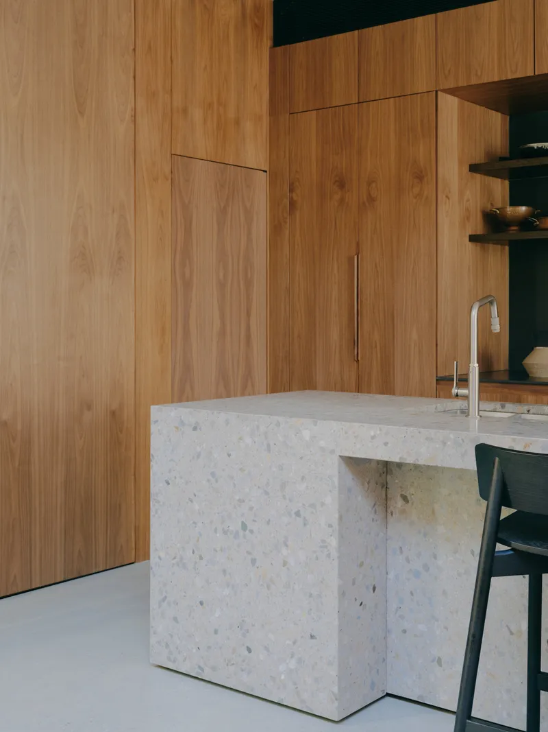 Terrazzo kitchen island detail against a walnut veneer cabinet wall with integrated shelving