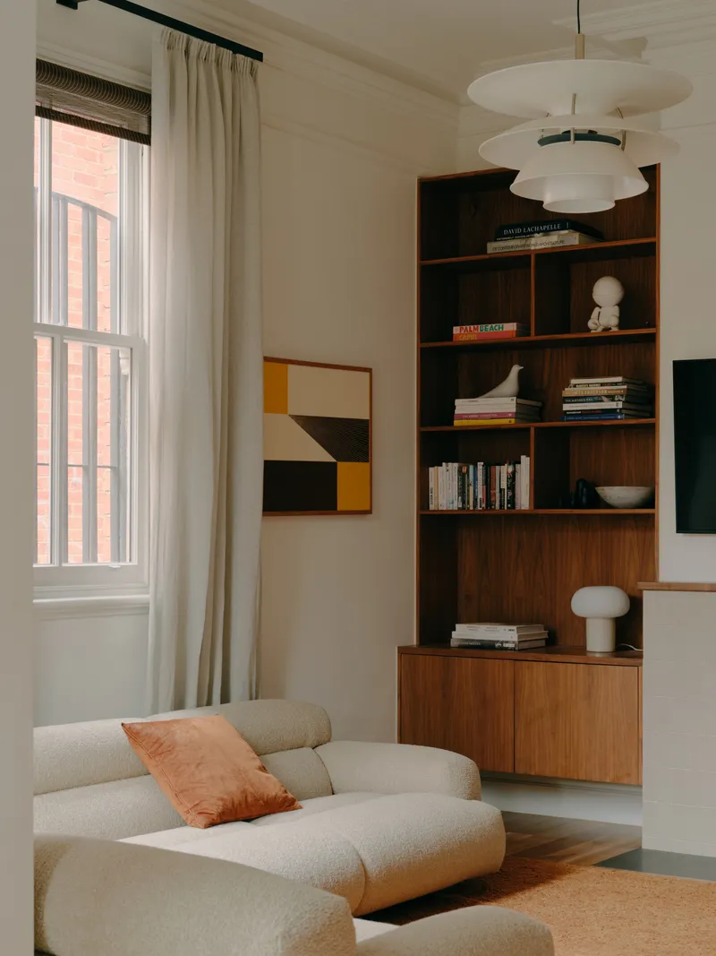 Living room with tall walnut shelving unit and tiered pendant light fixture above sectional seating