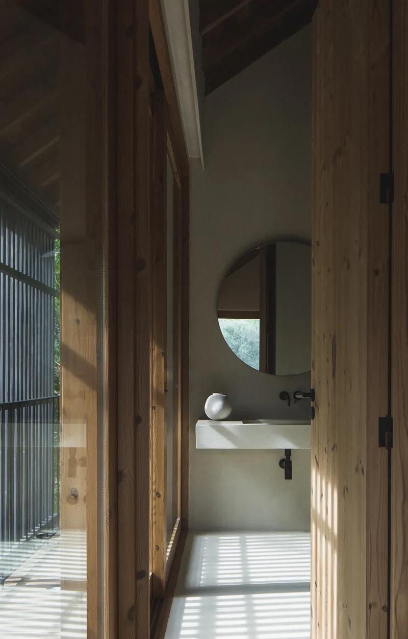 Bathroom entrance with timber doorframe and striped shadow pattern cast across polished concrete floor