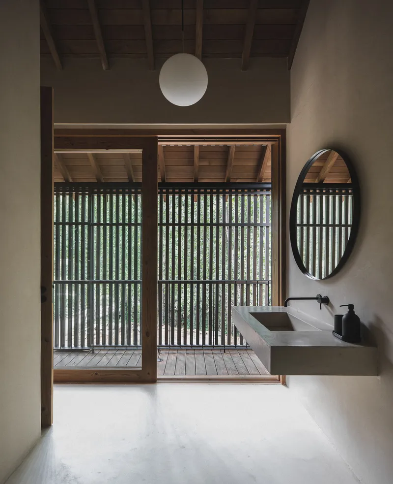 Bathroom with concrete sink and oval mirror facing timber-framed sliding doors opening to slatted screen balcony