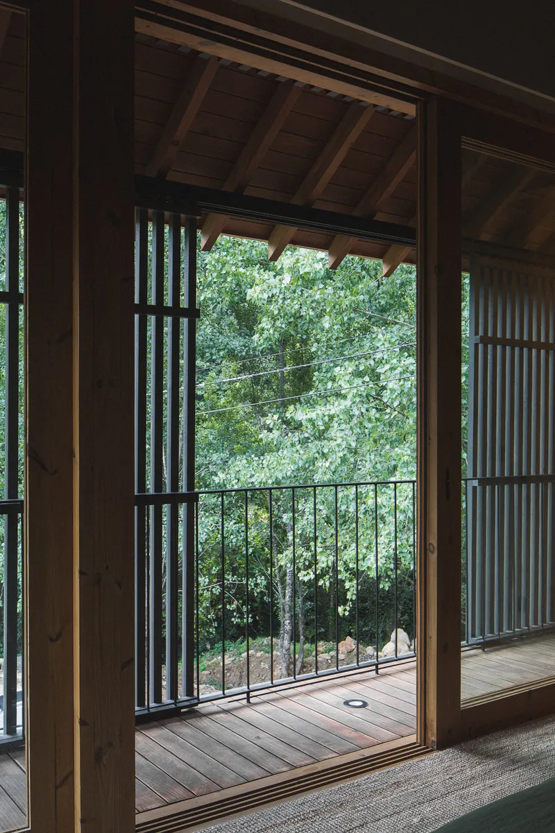 View through open timber doorway to wooden deck with metal railing overlooking green foliage