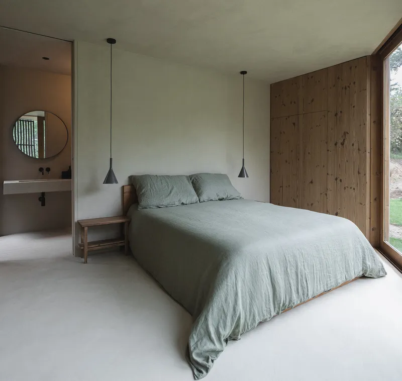 Bedroom with timber-clad wall and ensuite bathroom visible through doorway with circular mirror