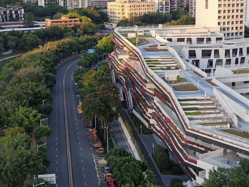 Aerial view of the cascading terraced facade with planted balconies alongside a tree-lined road