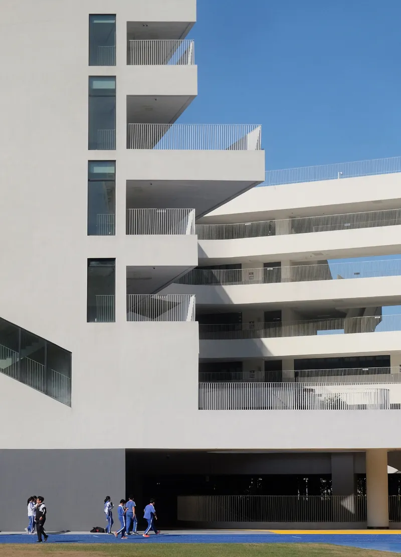White facade with recessed balconies and vertical louvres as students walk across blue pavement below