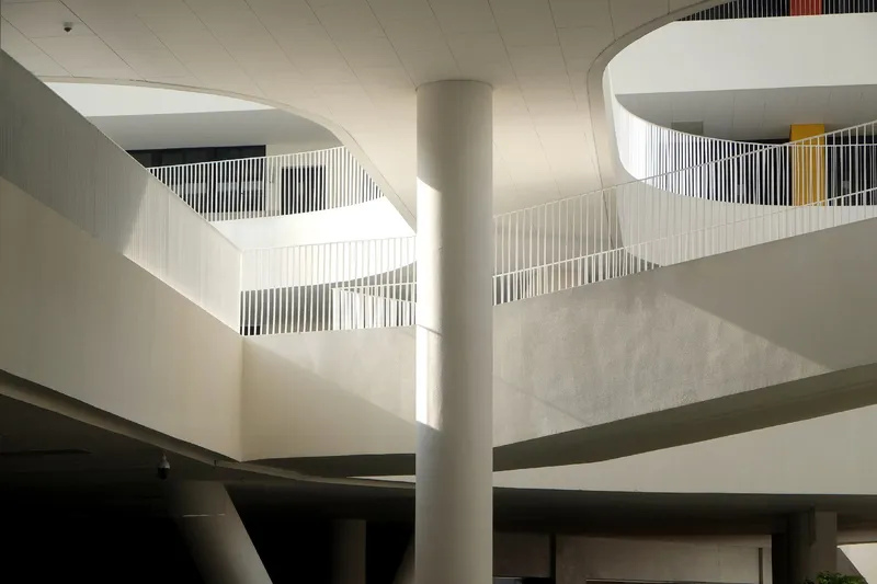 Interior atrium with curved balconies and vertical slat railings in soft morning sunlight