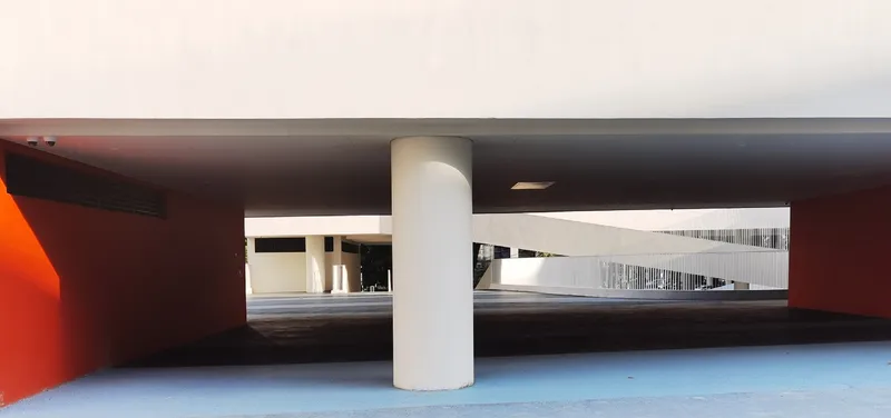 Covered parking level with cylindrical columns and orange accent wall under a dark soffit