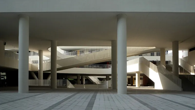 Covered plaza with round columns framing views of multilevel ramps and balconies in afternoon light