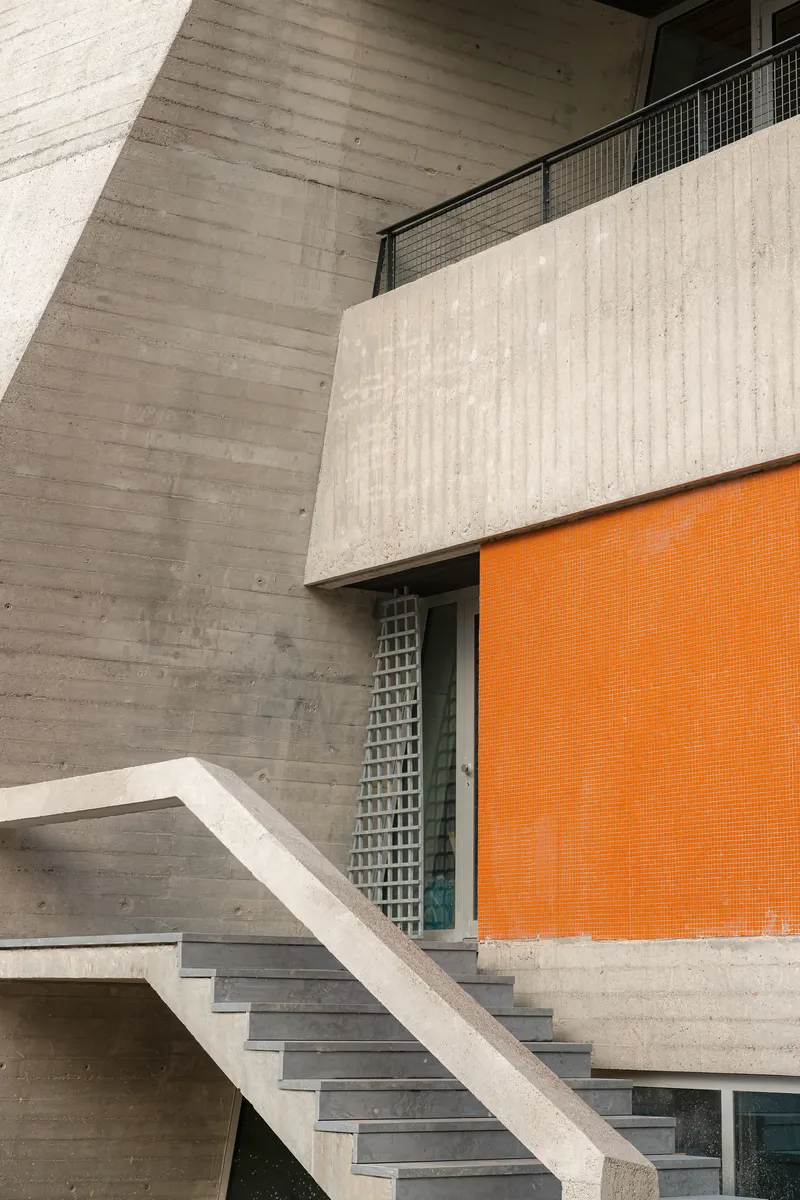 Board-formed concrete staircase and balcony with orange tile wall and metal mesh screen in the atrium