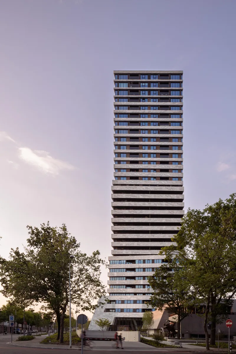 Stacked facade of alternating solid and glazed bands viewed from across the street at dusk