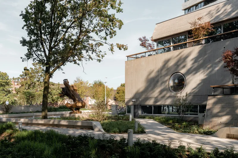 Entrance facade with circular porthole window and planted courtyard with sculpture under dappled tree shadow