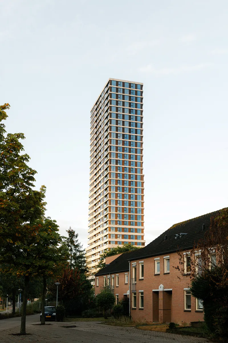 Slender residential tower rising above low-rise brick houses and mature street trees