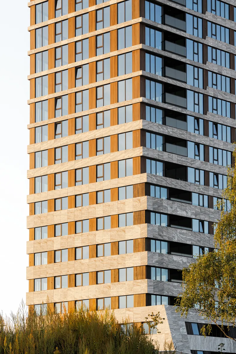 Tower facade with alternating beige and orange panels beside recessed balconies under autumn light