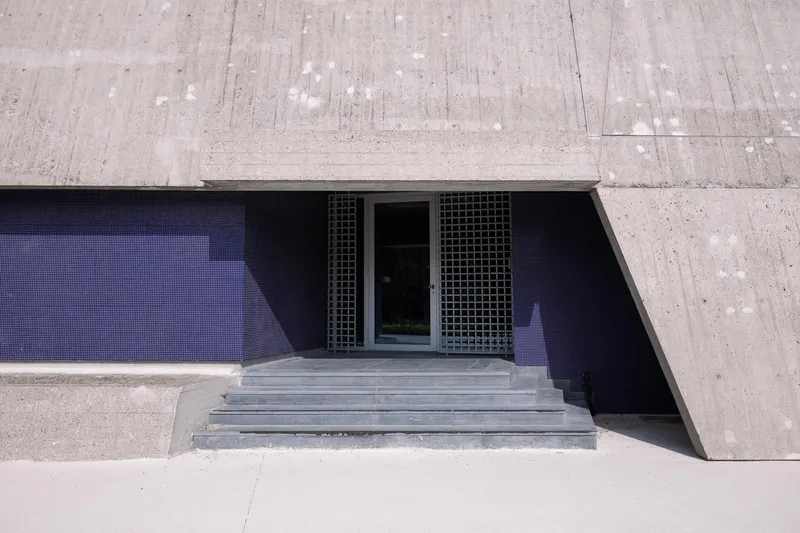 Sunken concrete entry stairs leading to recessed doors with metal grilles under bright midday sun
