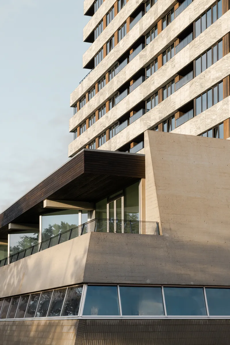 Angled concrete facade with ribbon windows above a timber-clad canopy and pedestrian ramp