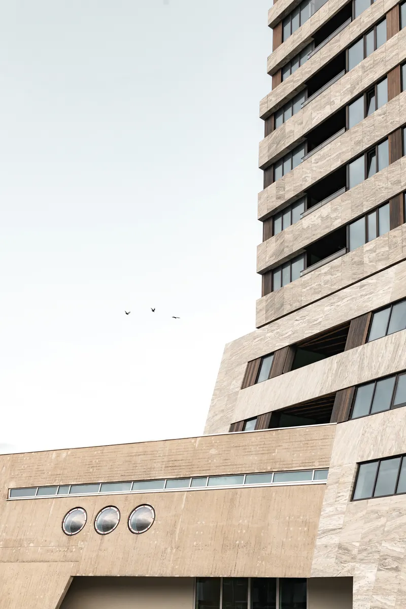 Stone-clad facade with three circular porthole windows and birds flying across the pale sky