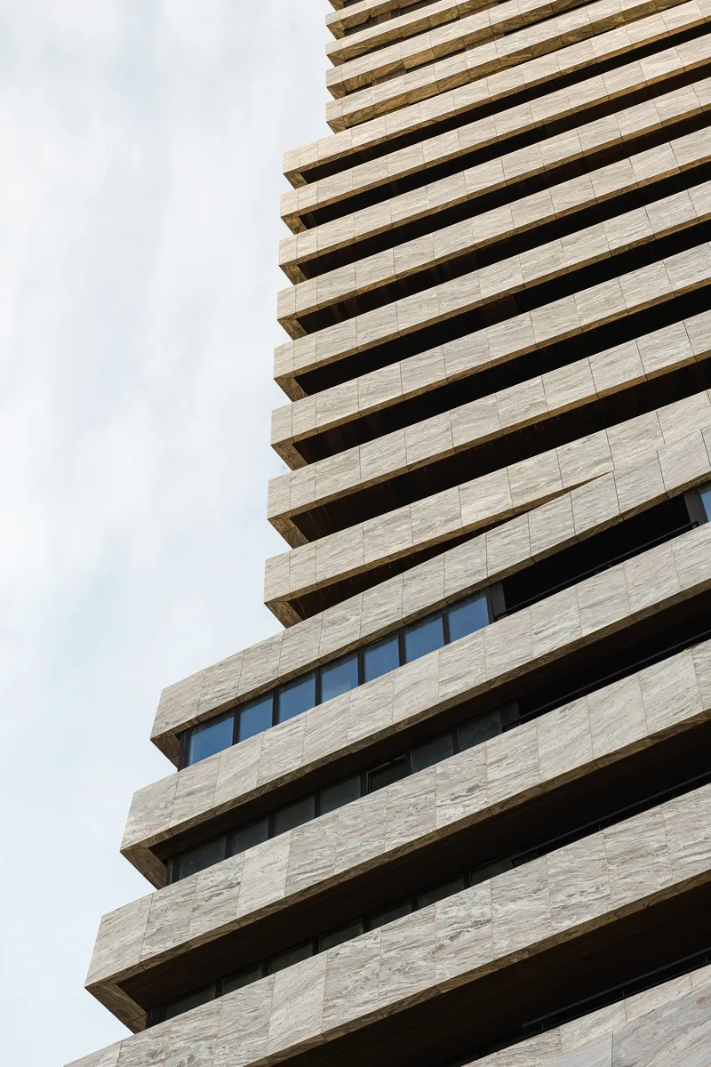Upward view of stacked balconies with deep soffits and horizontal stone cladding against cloudy sky