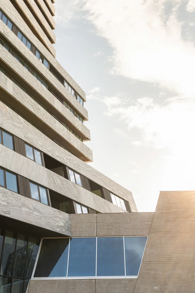 Tower corner showing layered stone balconies above an angled glass bay at the podium level