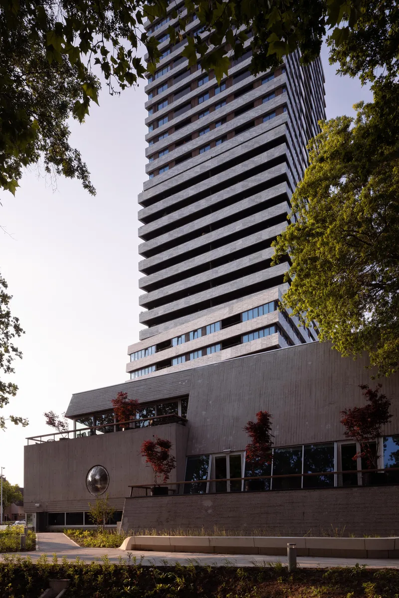 Dusk view of the tower above a landscaped terrace with red-leaved maples framing the entrance