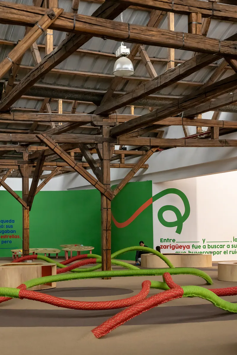 Interior exhibition space with exposed timber truss ceiling and bright green rope installations on the polished floor