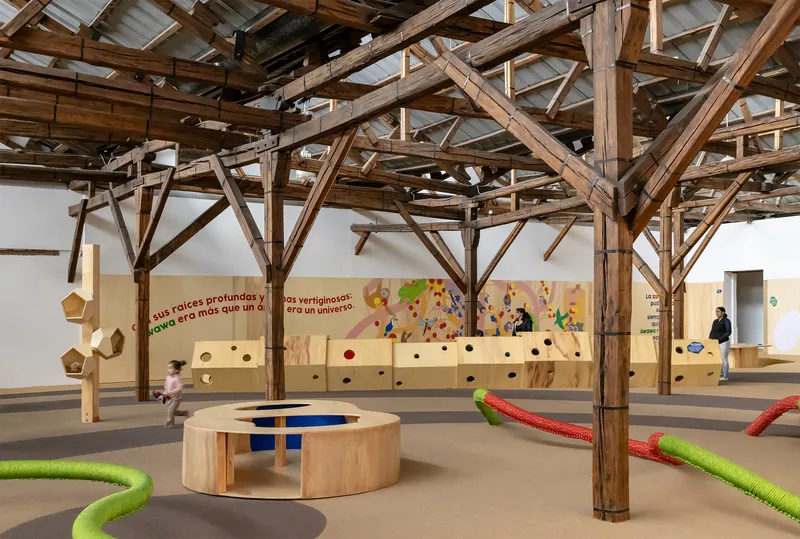 Wide view of the gallery showing timber columns, circular plywood seating and children running across the floor