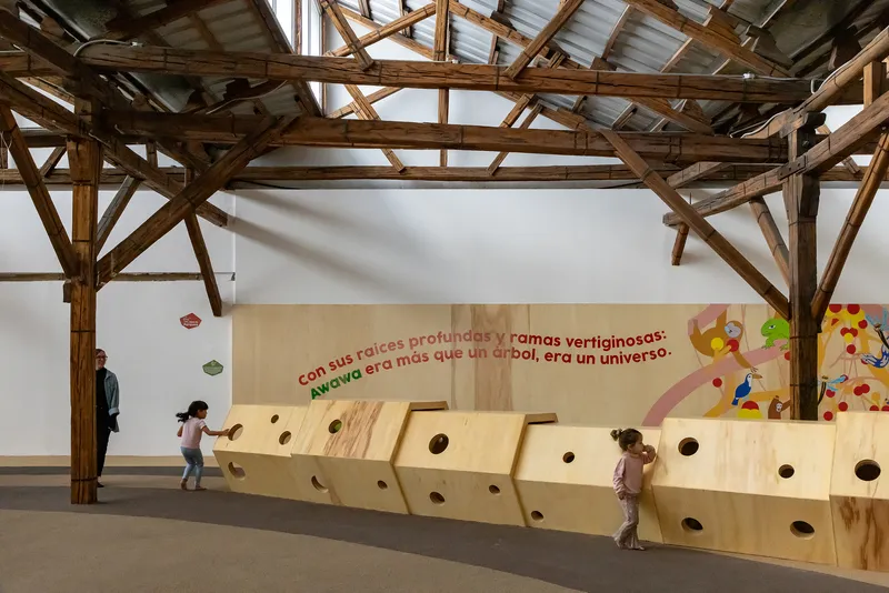 Plywood wall with circular portholes where two children peer through at different heights