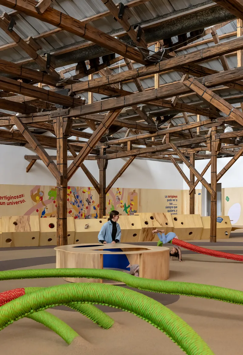 Interior view of exposed timber truss ceiling with translucent panels above play area with children