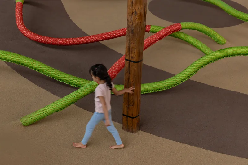 Child walking past timber column with green and red rope tubes extending across floor