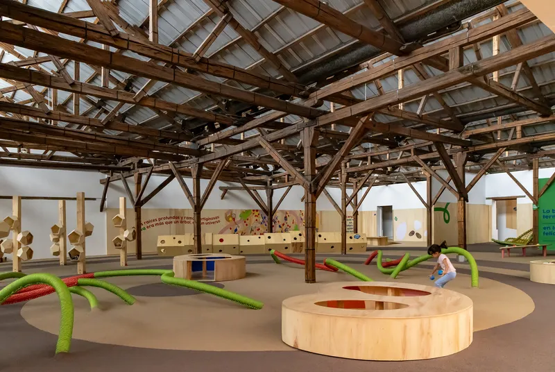 Interior showing circular plywood seating with children playing among rope installations under timber frame