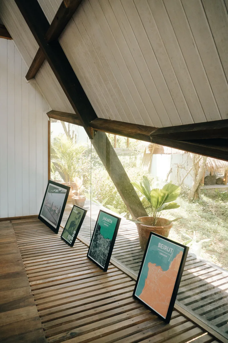 Slatted timber floor supporting a row of framed posters and a potted plant beneath angled beams