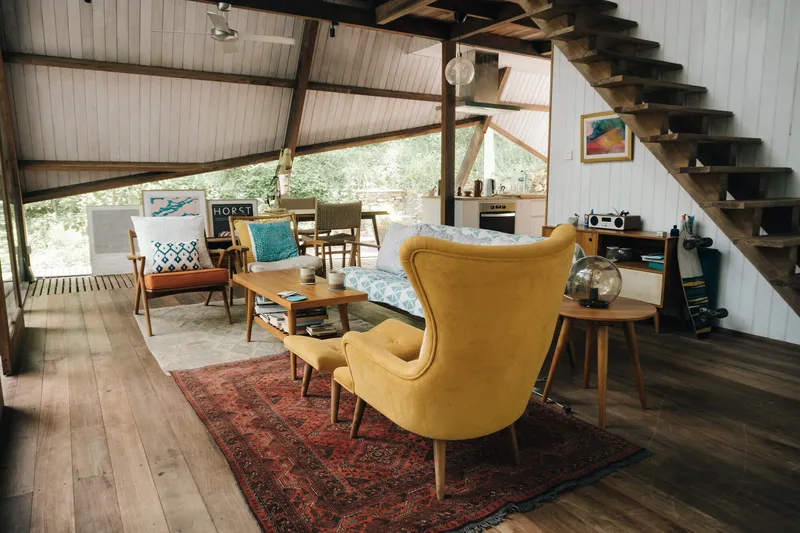 Living area with timber flooring, patterned rug and open stair beneath diagonal bracing