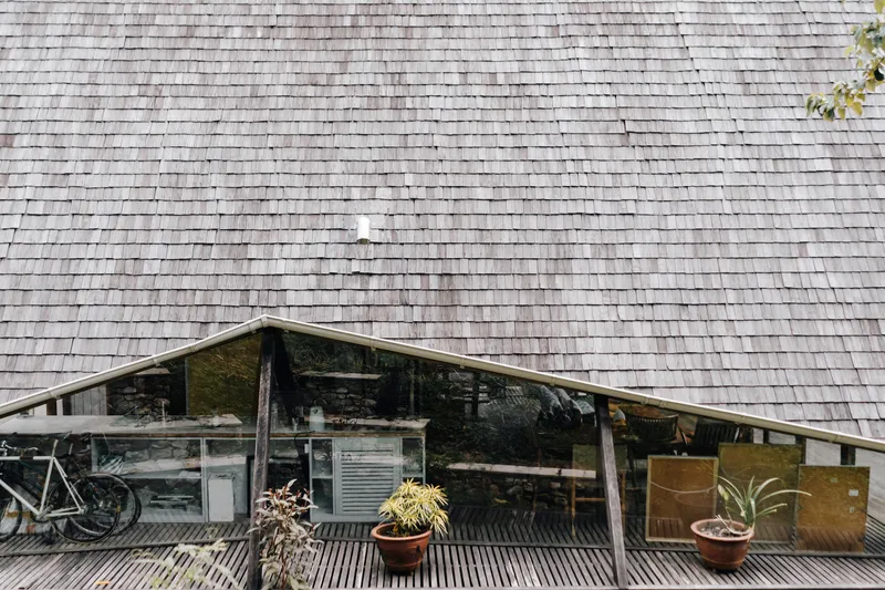 Weathered wooden shingle roof above a recessed terrace with horizontal slat flooring and potted plants