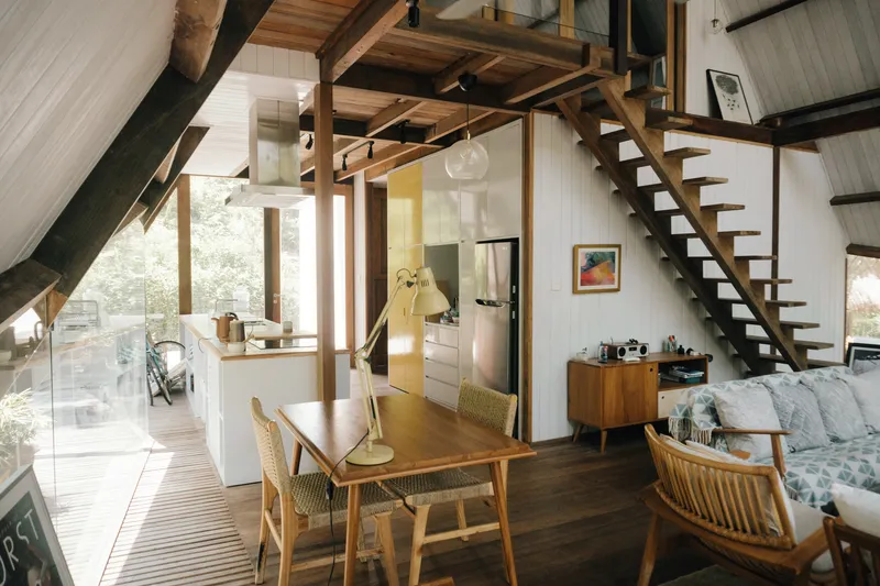 Double-height interior with exposed timber beams, open staircase and dining area beneath pendant light