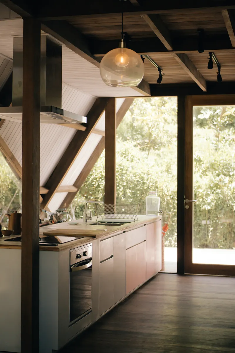 Kitchen island with white cabinetry beneath exposed timber beams and glass pendant fixture looking toward garden