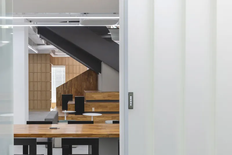 View through office doorway framing the timber amphitheater seating and angular black steel staircase beyond