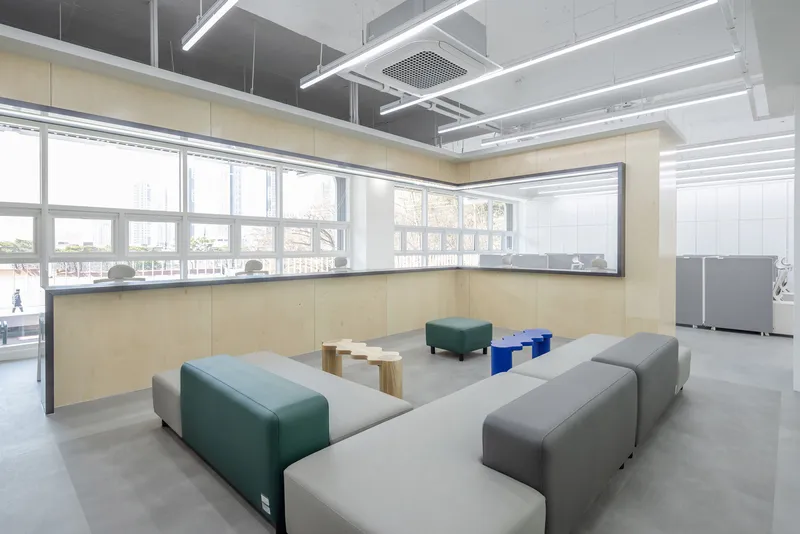 Open lounge area with modular seating, light wood paneling and exposed ceiling with linear fixtures