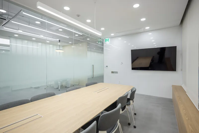 Conference room with long timber table, translucent glass partitions and suspended linear lighting