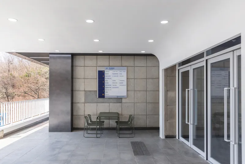 Covered outdoor terrace with metal seating, tiled floor and information board on textured wall