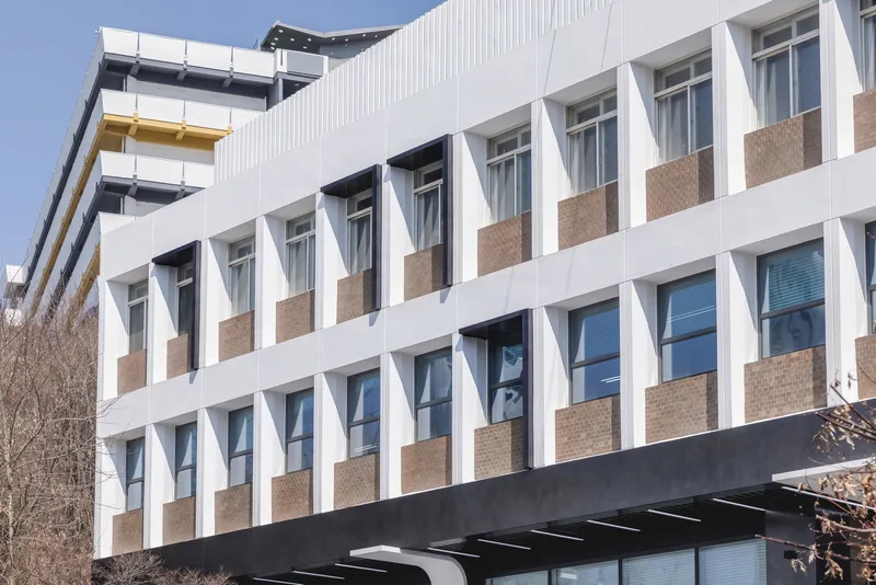 Street facade with zigzag white sunshades alternating with tan brick panels under a clear sky